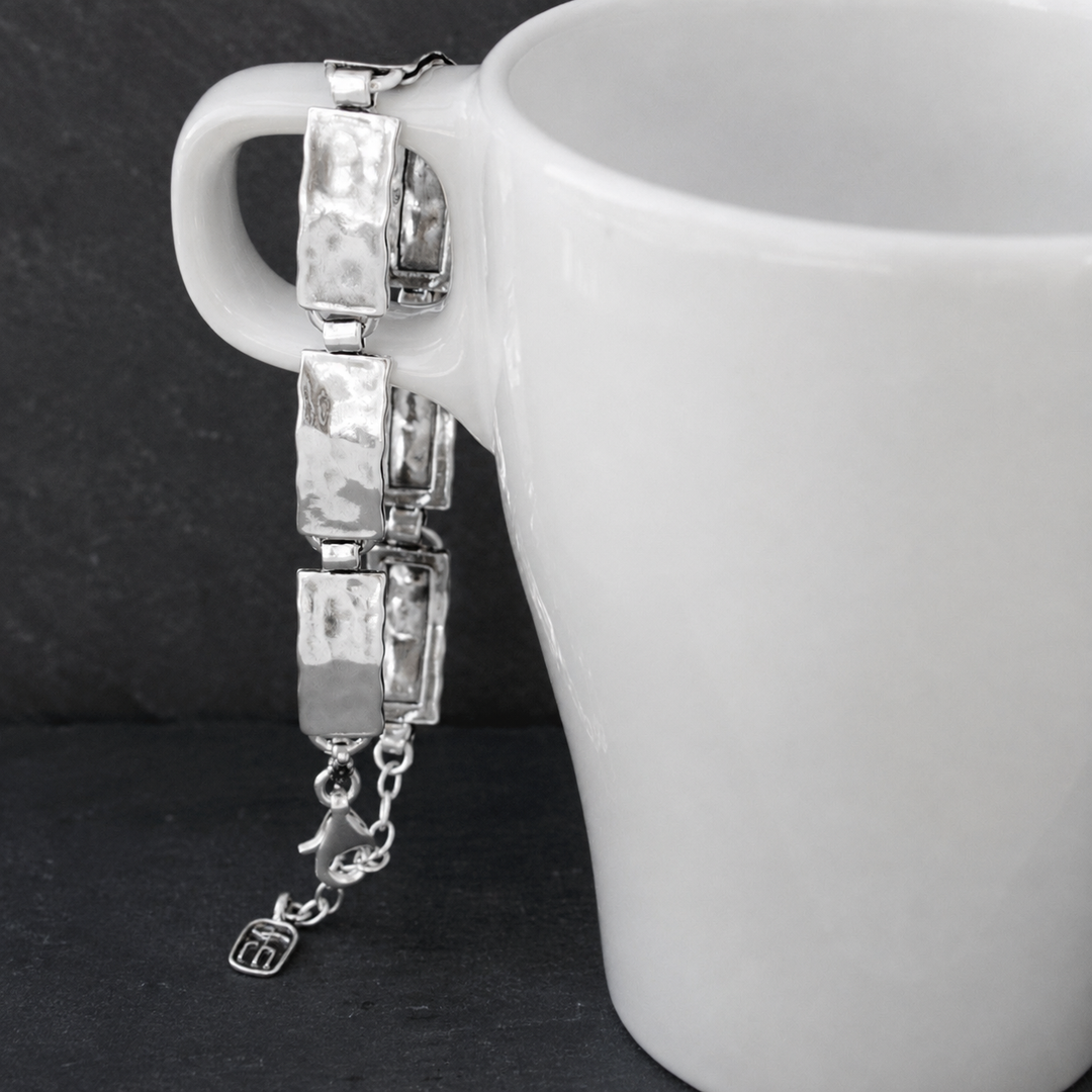 Everyday Sterling Bracelet with hammered rectangular sterling silver links, clasp, extender chain, and RockHill charm hanging from a white ceramic vessel on a dark background.