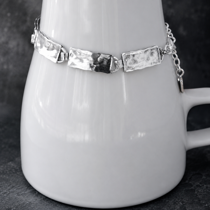 Everyday Sterling Bracelet with hammered rectangular sterling silver links, clasp, extender chain, and RockHill charm displayed around a white ceramic vessel on a dark background.