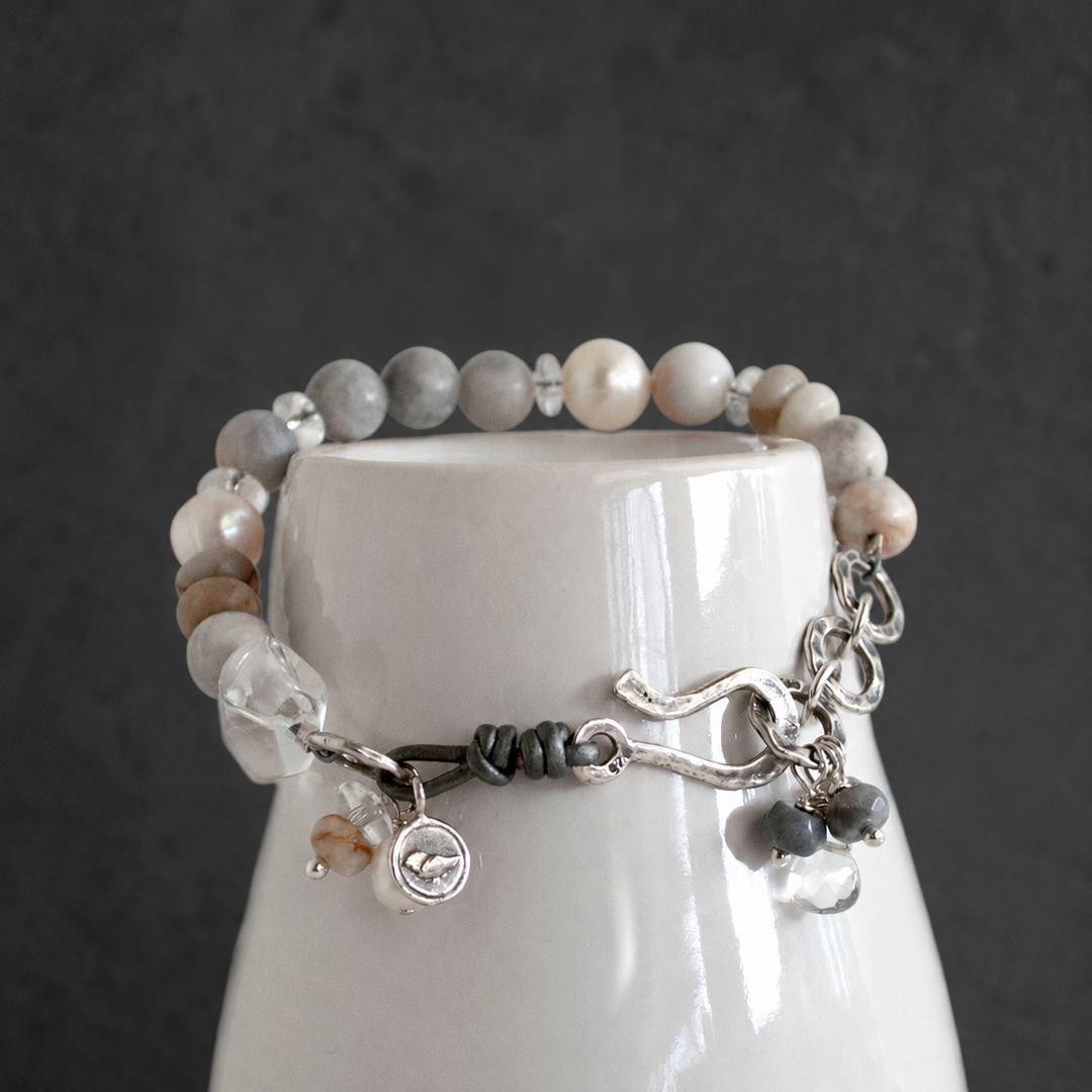 On the Rocks Bracelet with gray and white beads, freshwater pearls, clear quartz, and sterling silver accents displayed on a white ceramic vessel.