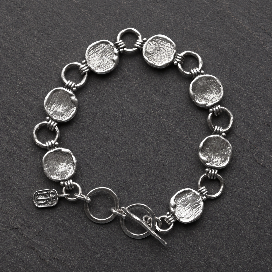 Cirque Link Bracelet in sterling silver with textured disc and circle links shown in a flat lay on dark slate.