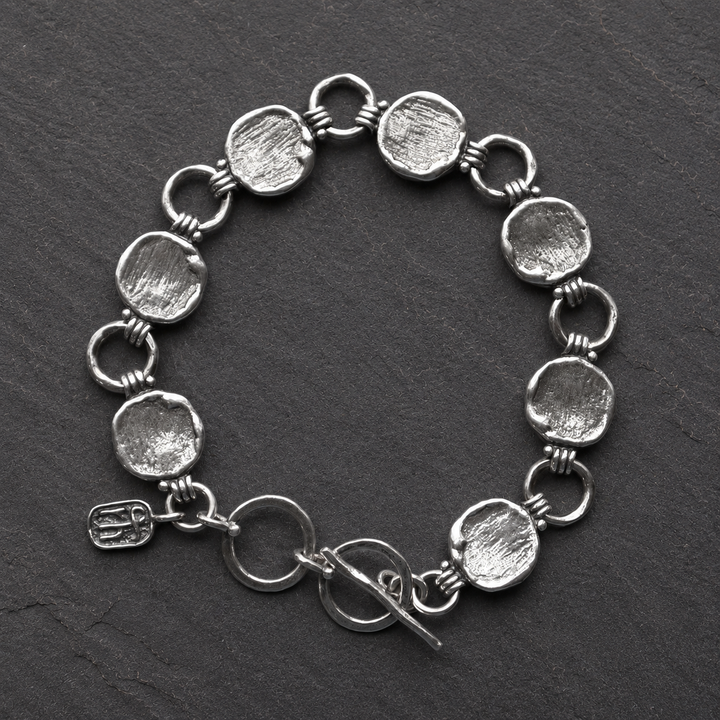 Cirque Link Bracelet in sterling silver with textured disc and circle links shown in a flat lay on dark slate.
