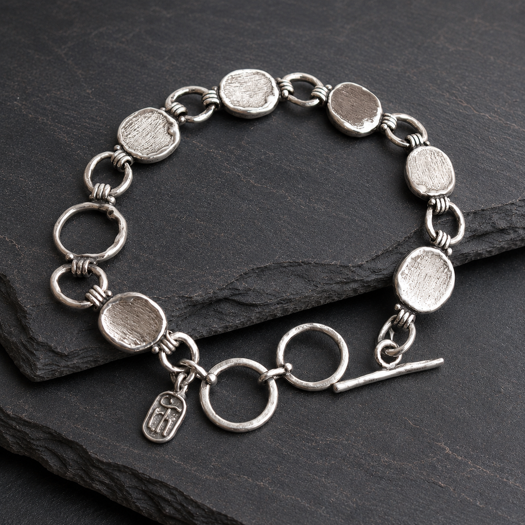 Cirque Link Bracelet in sterling silver with textured disc and circle links, adjustable toggle closure and RockHill charm on layered dark slate.