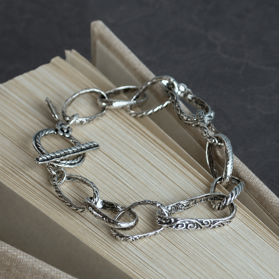 Hope Love Dream sterling silver link bracelet, shown in a circular flat lay on a dark gray background, with textured links and a toggle closure.