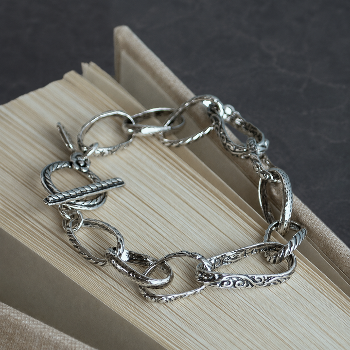 Hope Love Dream sterling silver link bracelet, shown in a circular flat lay on a dark gray background, with textured links and a toggle closure.