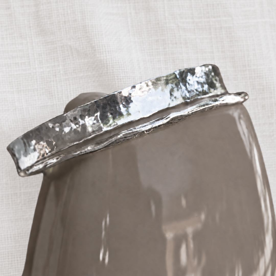 Modern Hammered sterling silver bangle bracelet displayed on a medium grey-brown ceramic vessel against a soft white linen background.