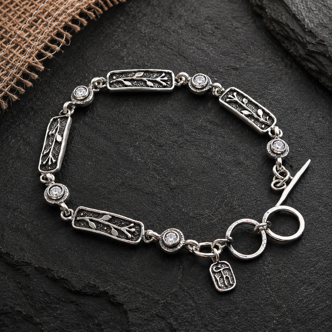 Sterling silver Glimmer bracelet with rectangular vine links and clear cubic zirconia on a dark slate background.