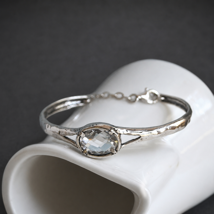 Brilliant Bracelet in sterling silver with an oval faceted clear CZ, cuff design, and safety chain on a white background.