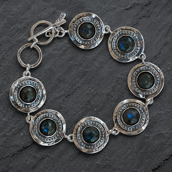 Crowned sterling silver labradorite bracelet with round bezel-set blue labradorite stones styled on a dark slate background.