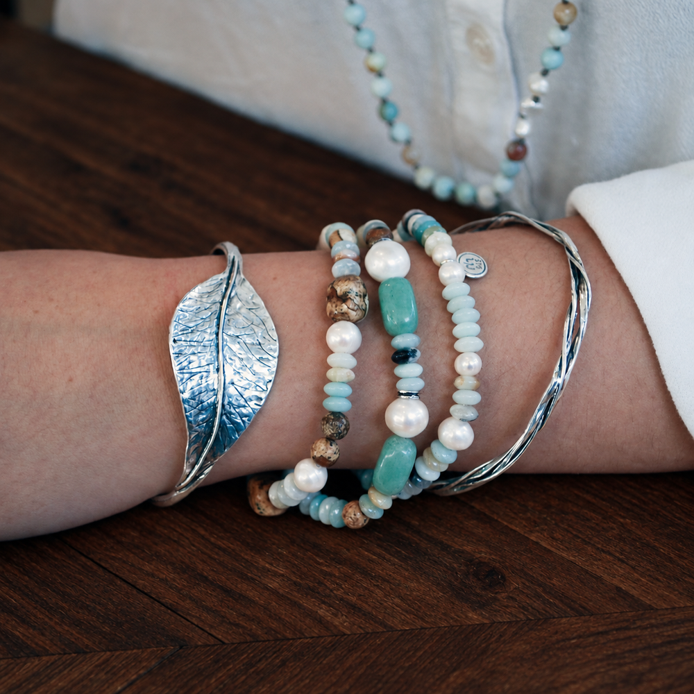 Peaceful Palette stretch bracelet stack with amazonite, freshwater pearls and picture jasper worn with sterling silver bangles on a dark chocolate wood surface.