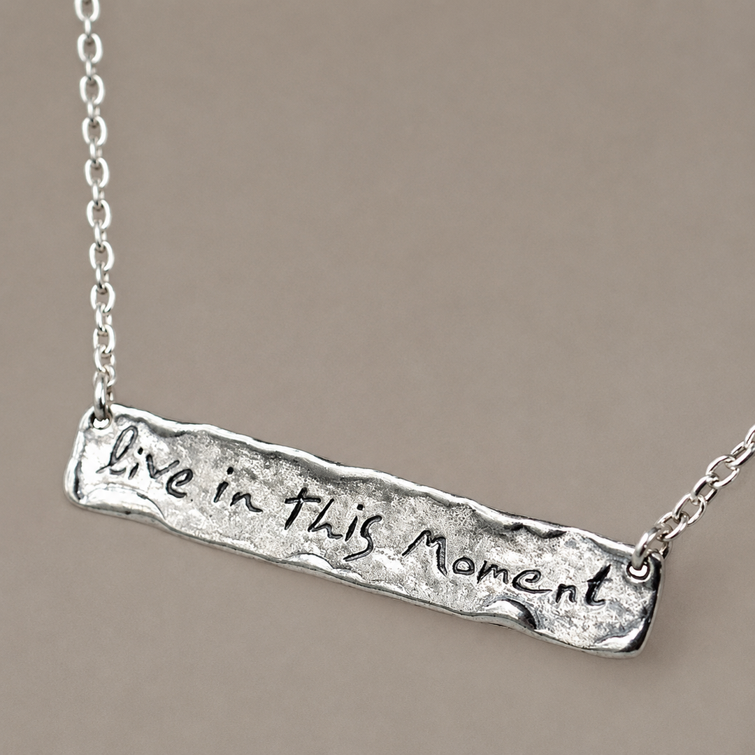 Live in This Moment sterling silver message necklace with rectangular pendant displayed on a soft grey brown background.