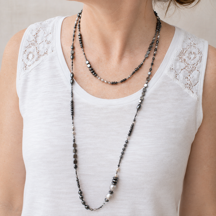 Jet Setter Chic Necklace with hematite, sterling silver, agate, and freshwater pearls worn long and layered over a white sleeveless top.