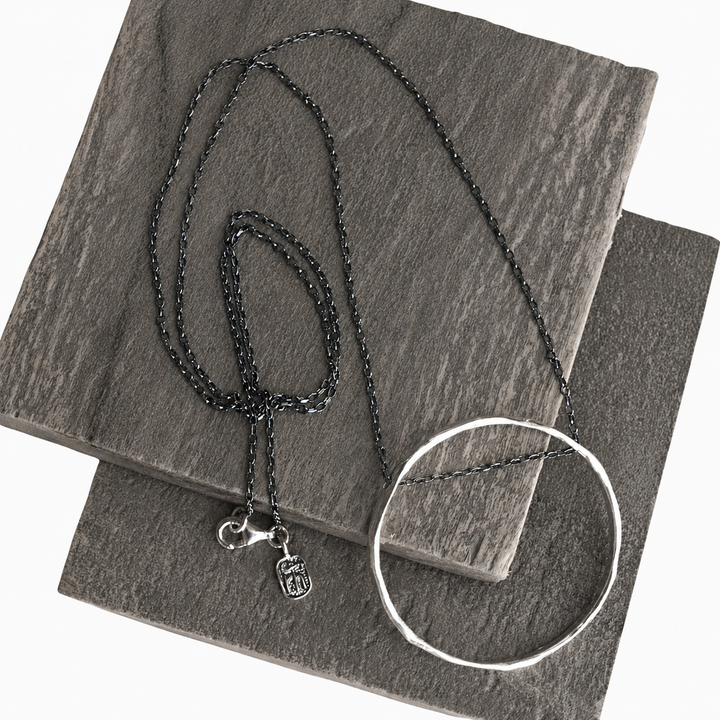 Full Circle Necklace with hammered sterling silver circle pendant and dark chain displayed on layered gray slate.