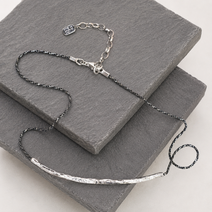 Raise the Bar Necklace with hammered sterling silver bar and dark twisted sterlng silver chain displayed on layered gray slate.