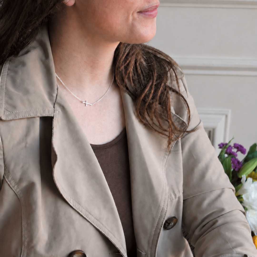 Sterling Silver Sideways Cross Necklace worn by a woman in a neutral trench coat against a soft warm greige background.