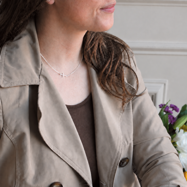 Sterling Silver Sideways Cross Necklace worn by a woman in a neutral trench coat against a soft warm greige background.