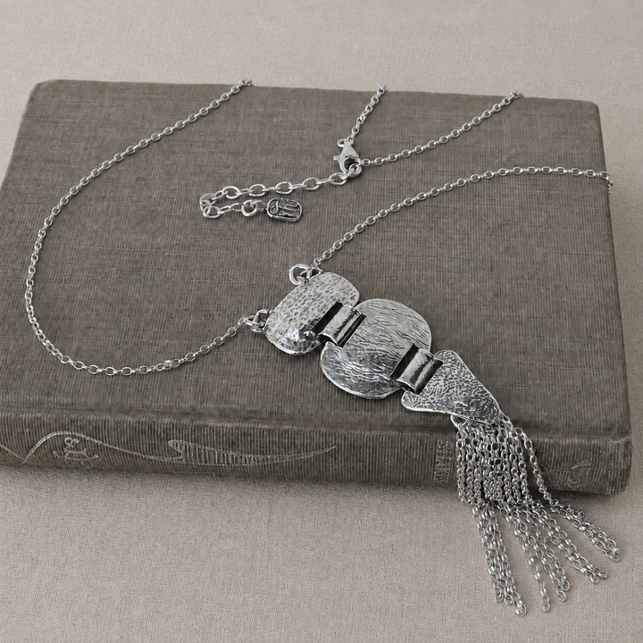 Meadowland Necklace N398, sterling silver textured pendant and chain tassel displayed on a gray-brown book with a light neutral background.