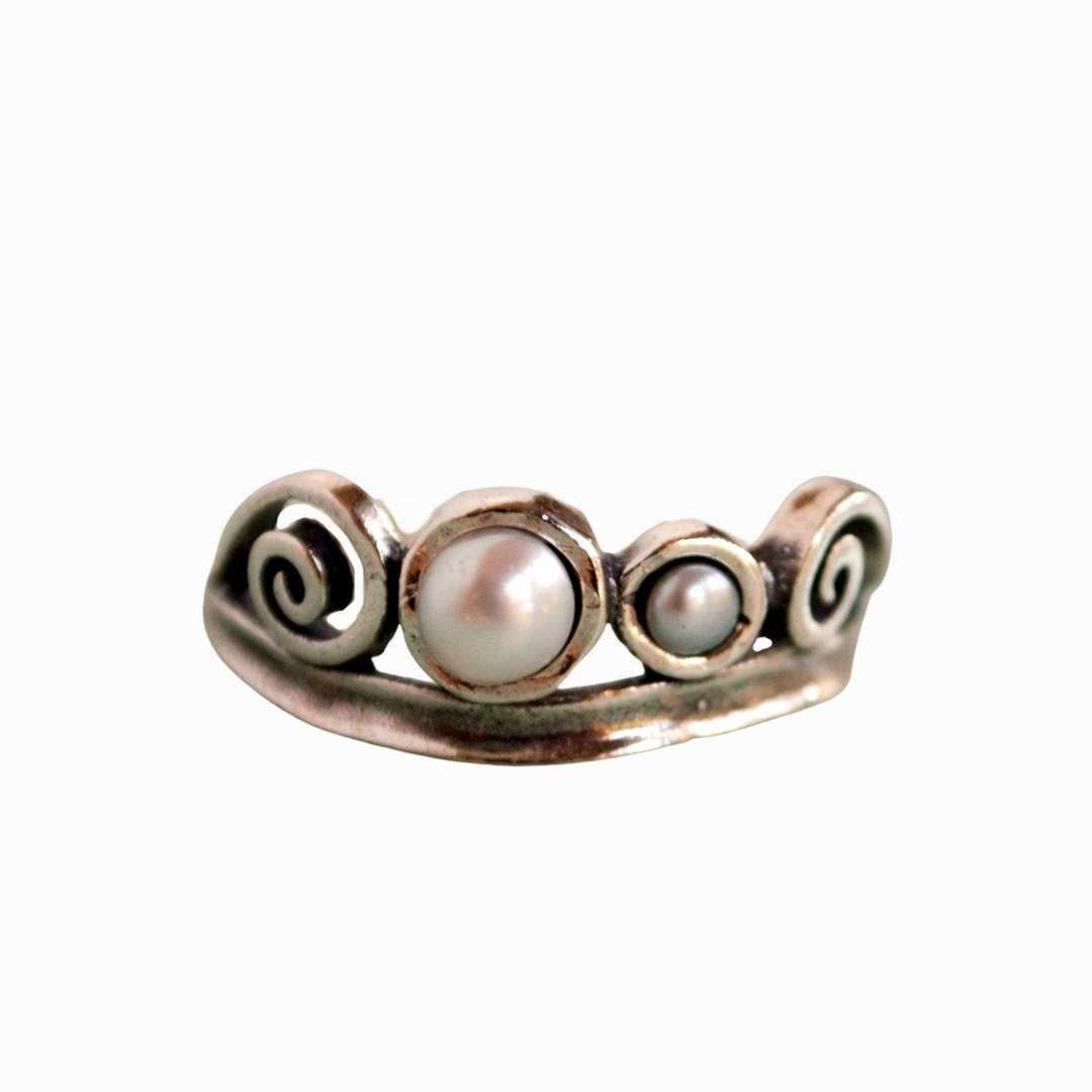 A sterling silver ring with three freshwater pearls set in a band with ornate details.