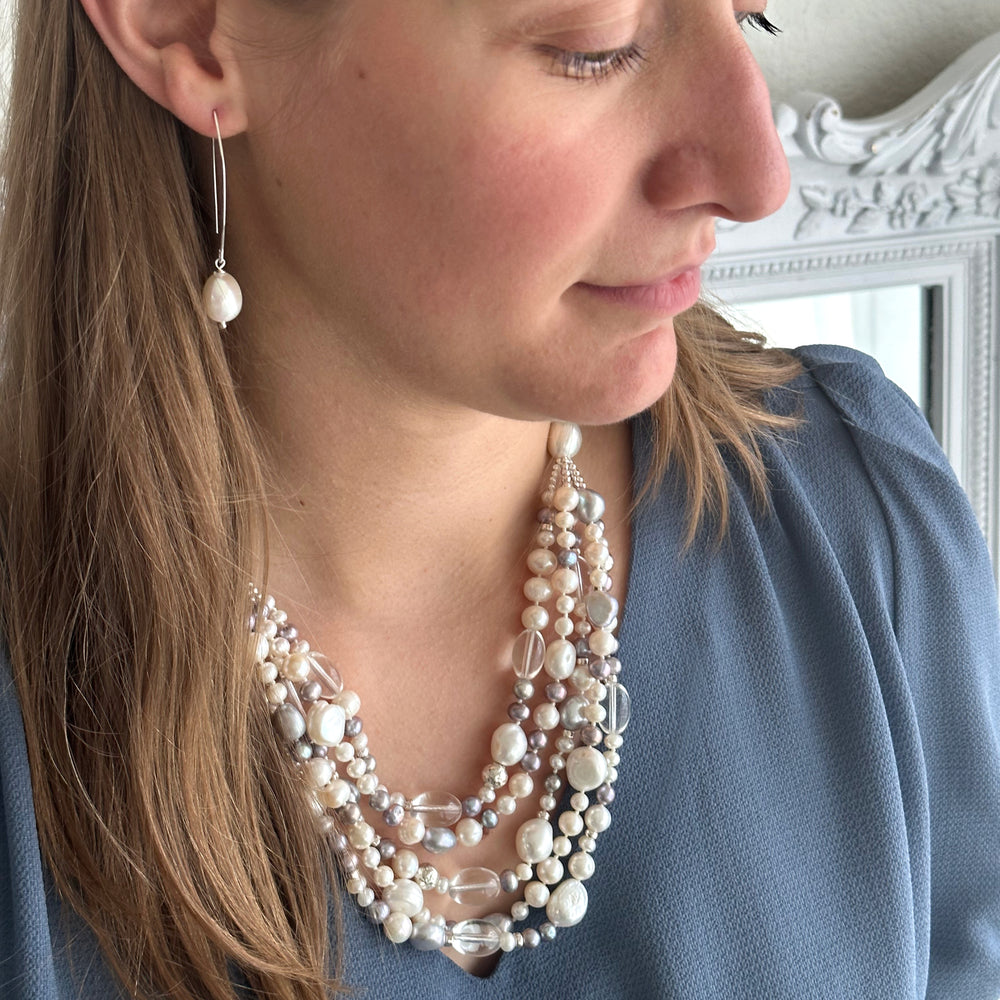 A model is shown wearting long sterling drop pearl earrings with a multi-strand pearl necklace. 