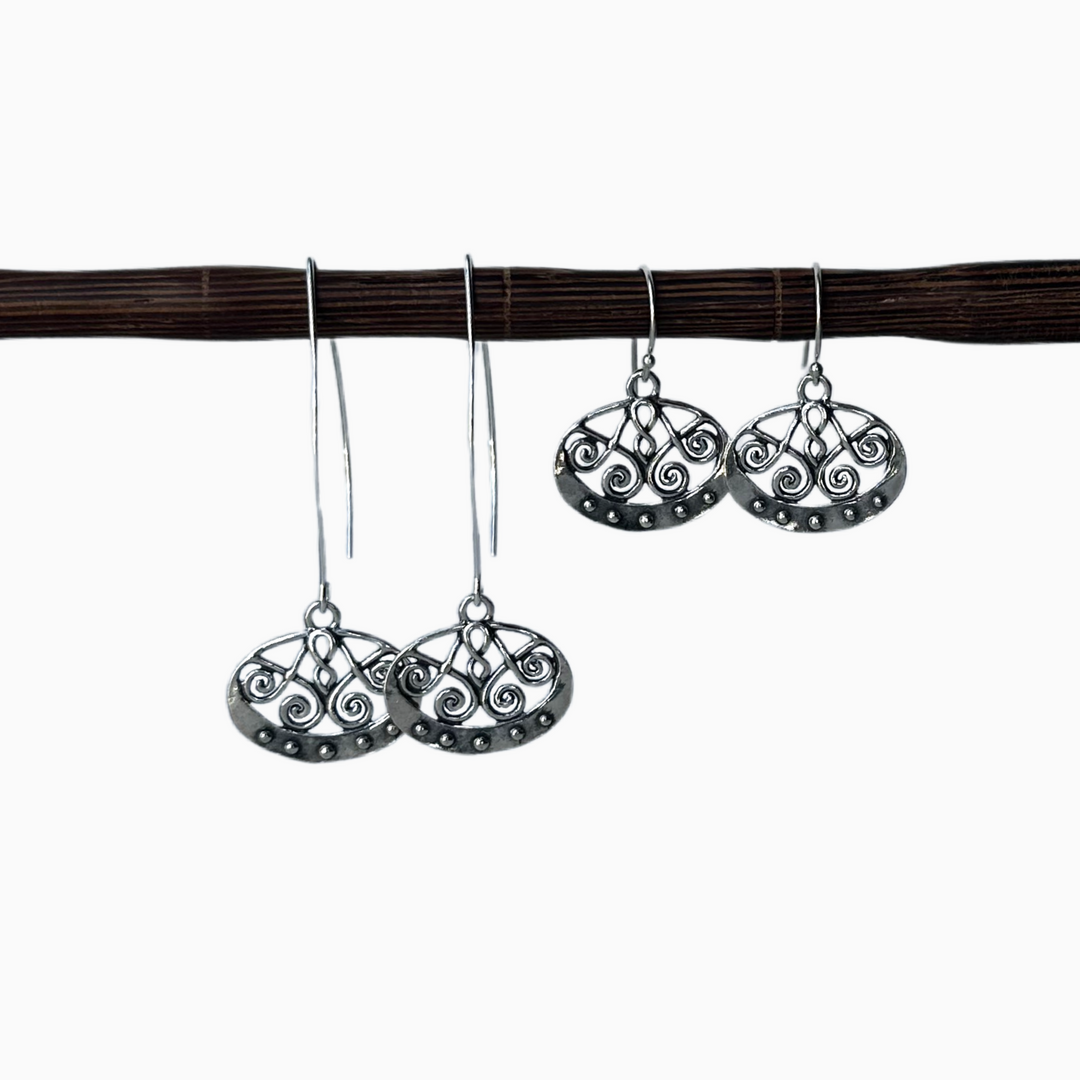 A pair of sterling silver dangle earrings with a geometric scroll design, displayed in both long and regular versions. Displayed on a wooden dowel with a white background. 