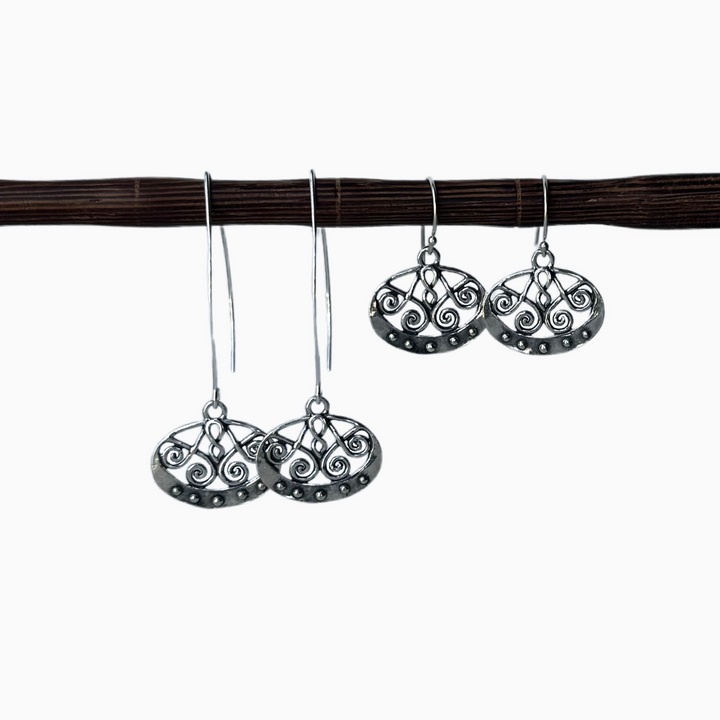 A pair of sterling silver dangle earrings with a geometric scroll design, displayed in both long and regular versions. Displayed on a wooden dowel with a white background. 