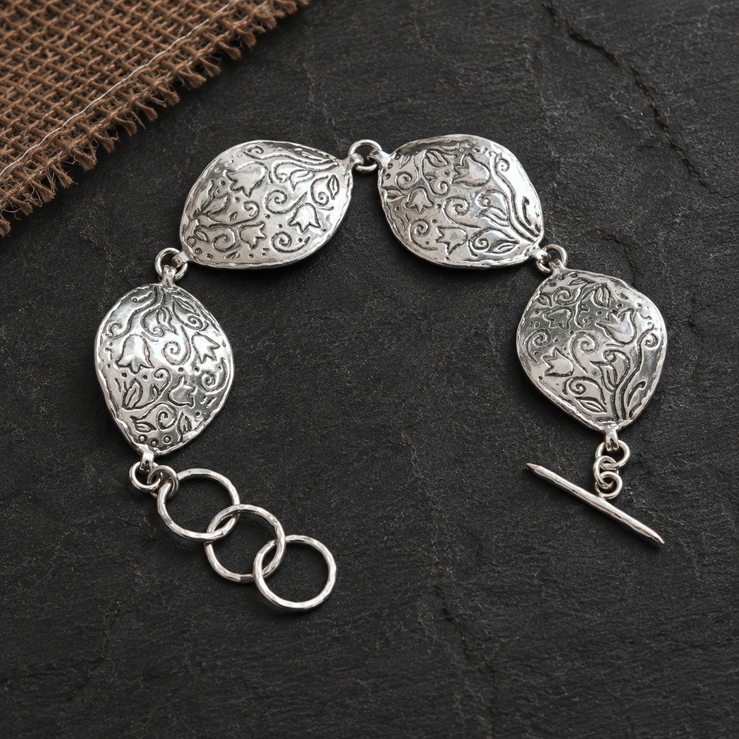 Sterling silver Petali Bracelet with four curved floral-patterned links and adjustable toggle clasp on a dark slate background.