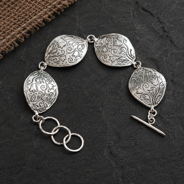 Sterling silver Petali Bracelet with four curved floral-patterned links and adjustable toggle clasp on a dark slate background.