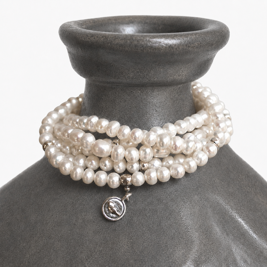 Party of Five Pearl Bracelet draped around a charcoal ceramic vessel, showing white freshwater pearls and sterling silver charm details.