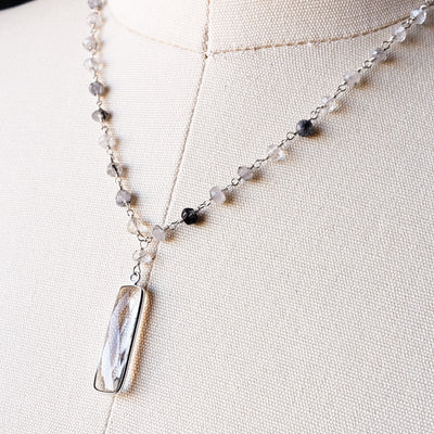 Necklace with faceted rutilated quartz is chain-linked, finished on genuine dark grey leather with a  faceted clear quartz pendant. The pendant measures 2" by 1/4" and the finished necklace is 15" with a built-in 2" extender.