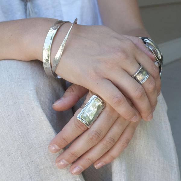 A silver bangle bracelet with a hammered texture and polished finish, is shown on a model. 