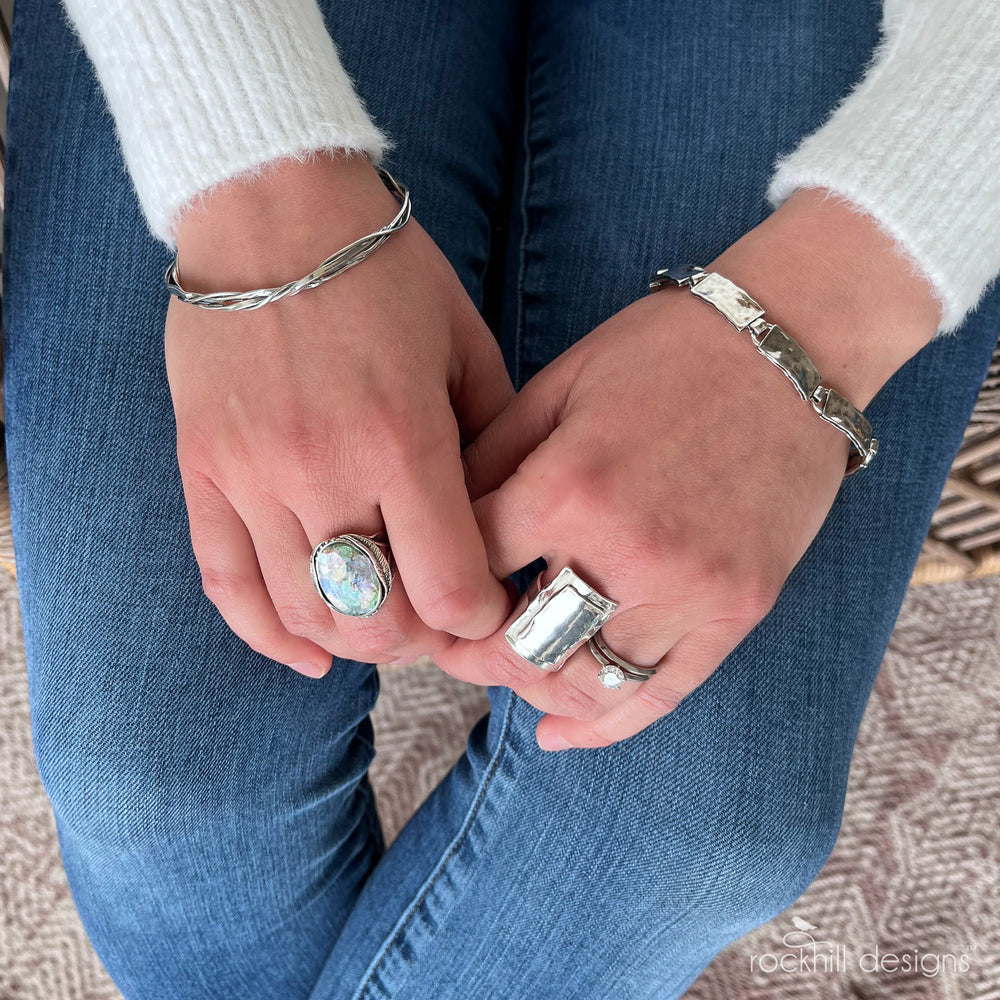 A sterling silver bracelet with links of slightly hammered texture is shown on a model. 