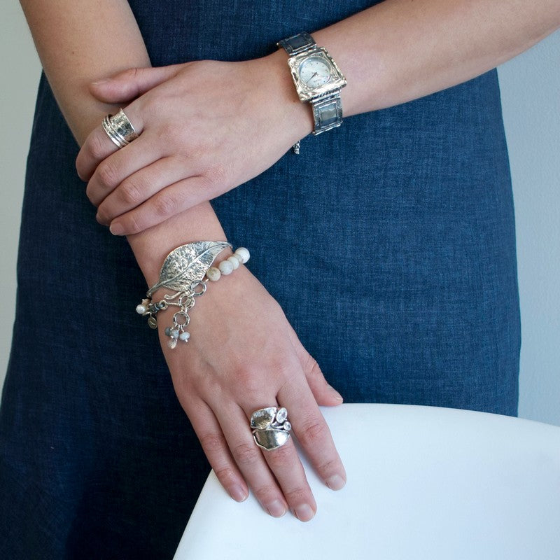 A bracelet with a mix of gray and white beads, pearls, and clear quartz, featuring a sterling silver clasp and leather detailing, is shown a model. 