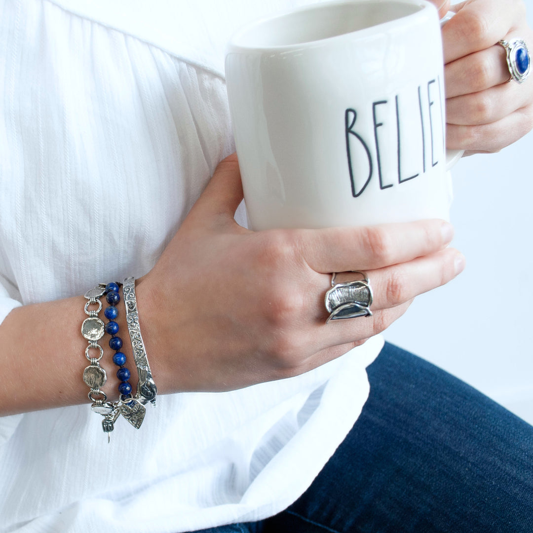 Bracelet consisting of smooth round 1/4" lapis beads on a brown adjustable silk cord. Features a heart dangle. Shown on a model. 