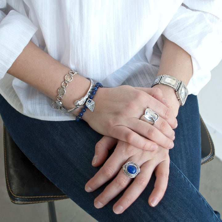 Bracelet consisting of smooth round 1/4" lapis beads on a brown adjustable silk cord. Features a heart dangle. Shown on a model.