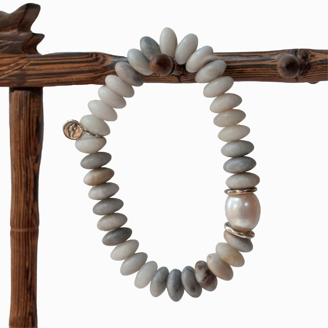 A stretch bracelet with smooth rondelle stone beads in shades of gray and white, featuring a lustrous cultured freshwater pearl and sterling silver accents, displayed on a wooden stick and white background.