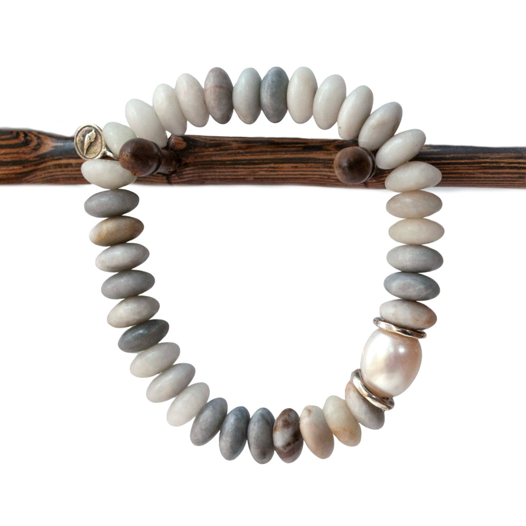 A stretch bracelet with smooth rondelle stone beads in shades of gray and white, featuring a lustrous cultured freshwater pearl and sterling silver accents, displayed on a wooden stick.