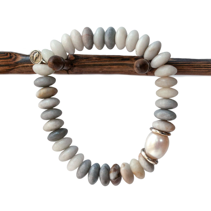 A stretch bracelet with smooth rondelle stone beads in shades of gray and white, featuring a lustrous cultured freshwater pearl and sterling silver accents, displayed on a wooden stick.
