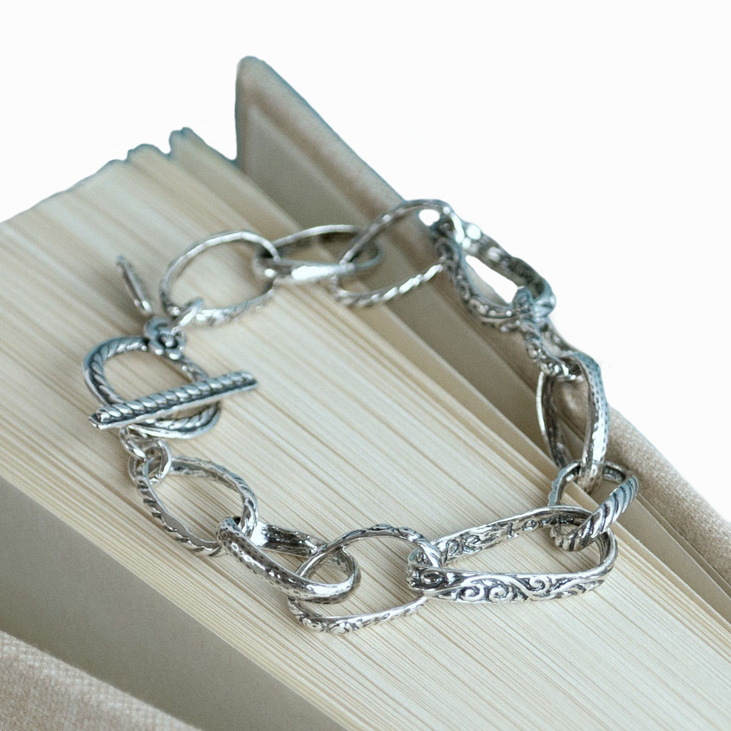 A sterling silver chain link design bracelet with an adjustable toggle clasp, displayed on a book. 