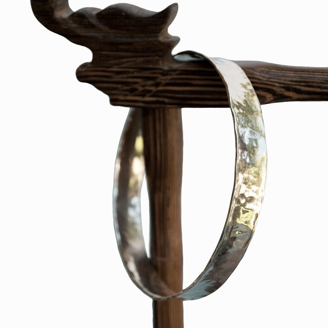 Hammered sterling silver bangle bracelet shown on a brown display piece. 