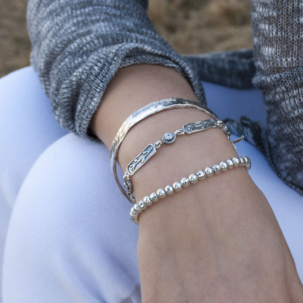 A single-strand sterling silver bracelet with bezel-set faceted clear CZs and an adjustable toggle closure. Shown on a model. 