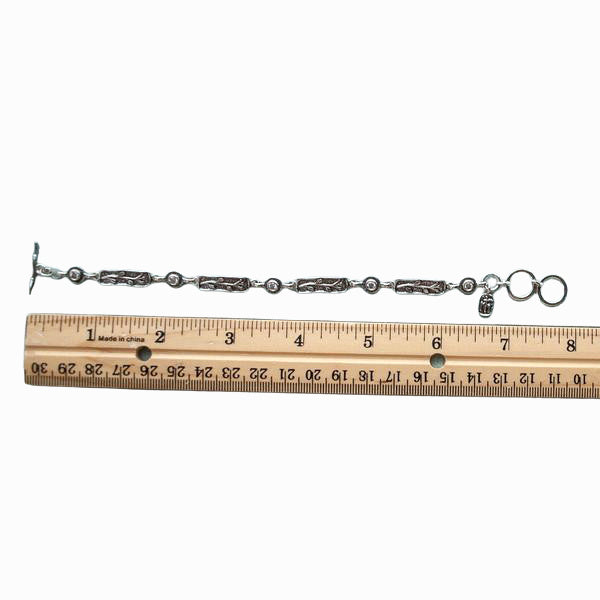 A single-strand sterling silver bracelet with bezel-set faceted clear CZs and an adjustable toggle closure. Shown by a ruler for scale. 