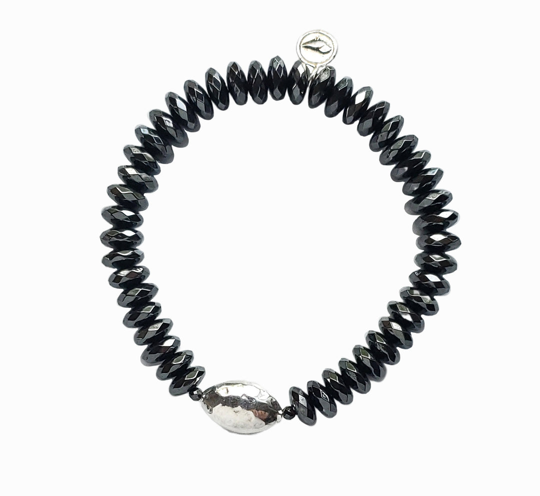A stretch bracelet with faceted hematite beads and a hammered sterling silver centerpiece bead, shown from above on a white background. 