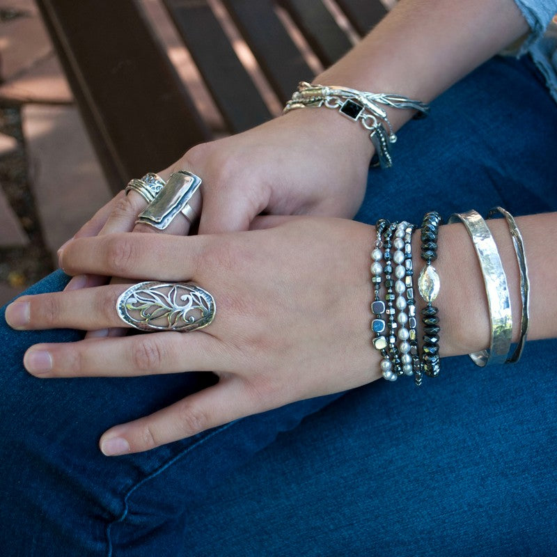 A stretch bracelet with faceted hematite beads and a hammered sterling silver centerpiece bead, shown on a model. 