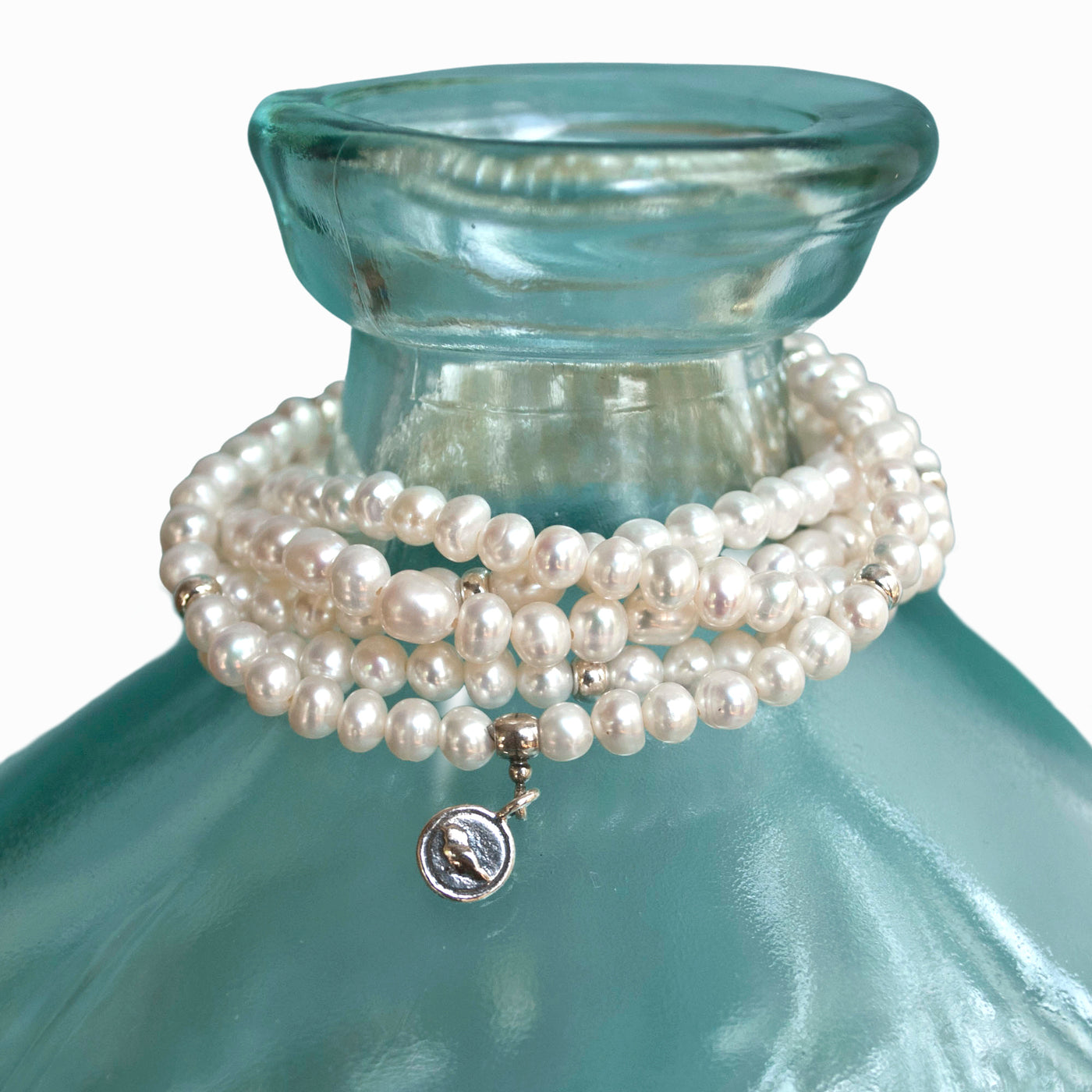 Five bracelets of white freshwater pearls with sterling accent beads are shown on a green glass bottle.  They are handcrafted in a stretch design to fit nearly everyone.