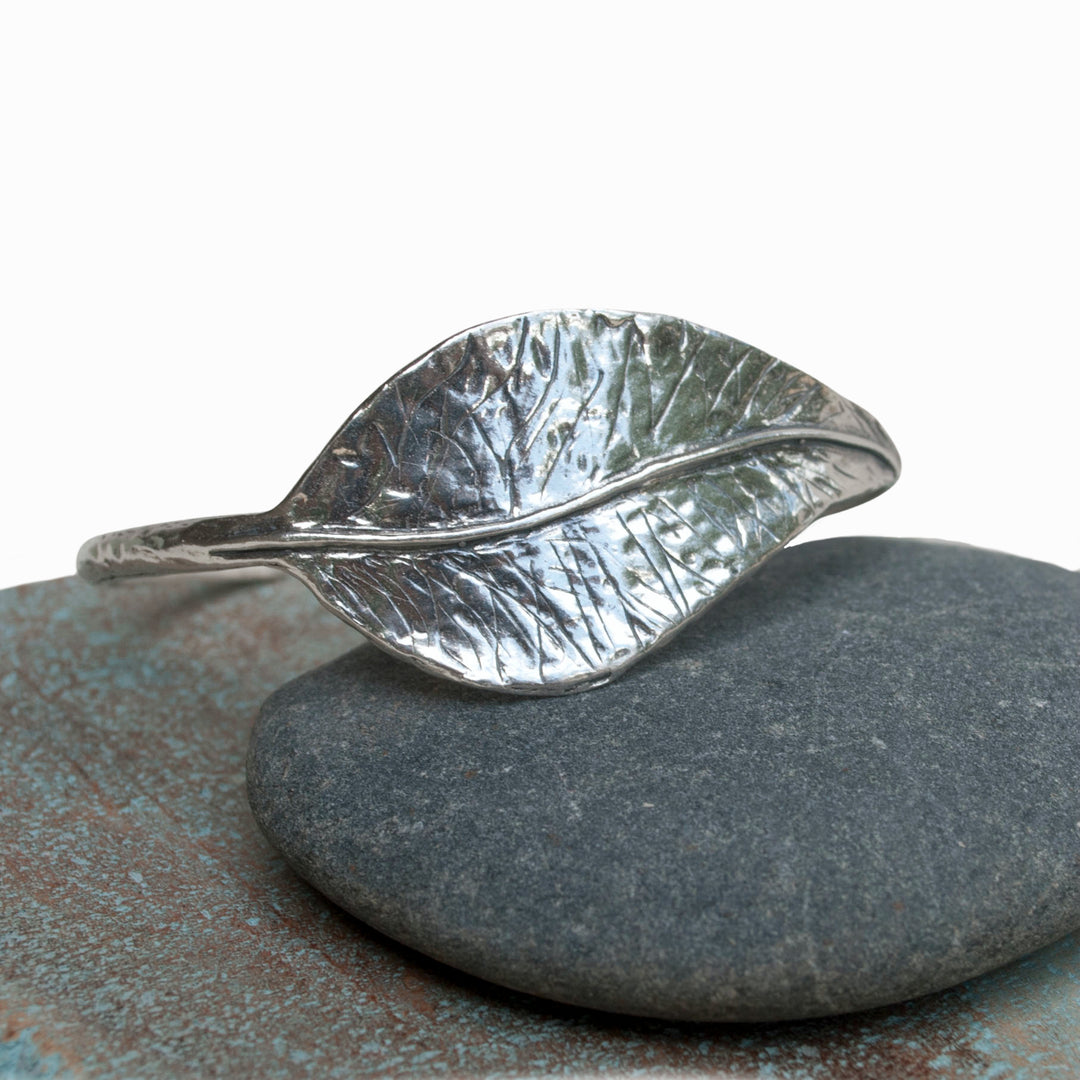 A sterling silver leaf cuff bracelet displayed on a grey stone. 