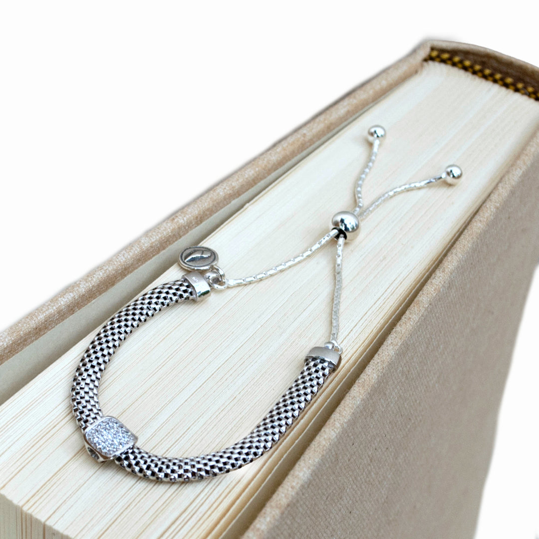 A sterling silver chain link design bracelet with a lobster clasp closure. Shown from above on a linen book. 