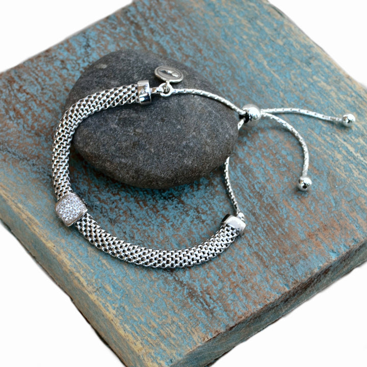 A sterling silver chain link design bracelet with a lobster clasp closure. Shown from above on wood tile.