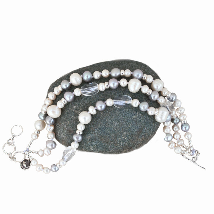 A multi-strand pearl bracelet with clear quartz and sterling silver accents, displayed on a gray stone.