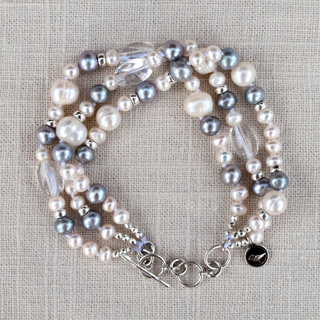 A multi-strand pearl bracelet with clear quartz and sterling silver accents, displayed on a linen from above. 