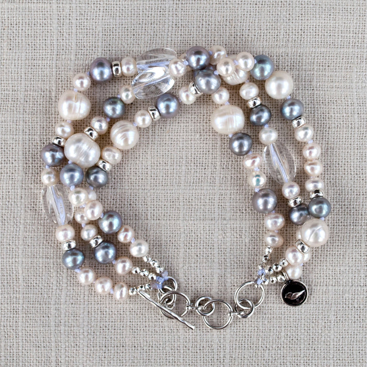 A multi-strand pearl bracelet with clear quartz and sterling silver accents, displayed on a linen from above. 