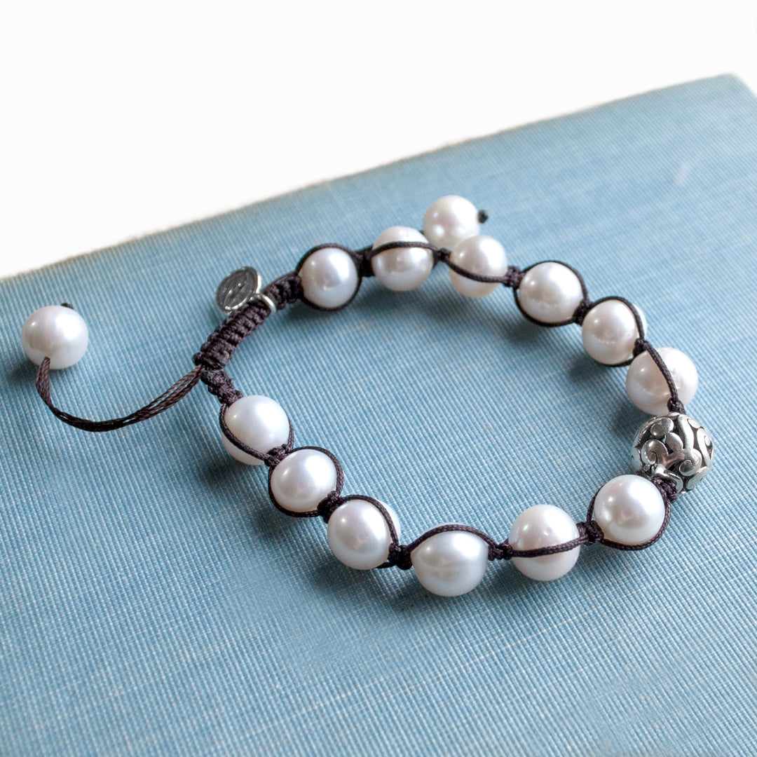 A single-strand pearl bracelet with a sterling silver focal bead and an adjustable closure, displayed on a blue linen surface.